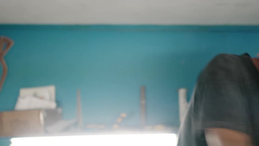 Man wearing a respirator sanding a surfboard on his small workshop