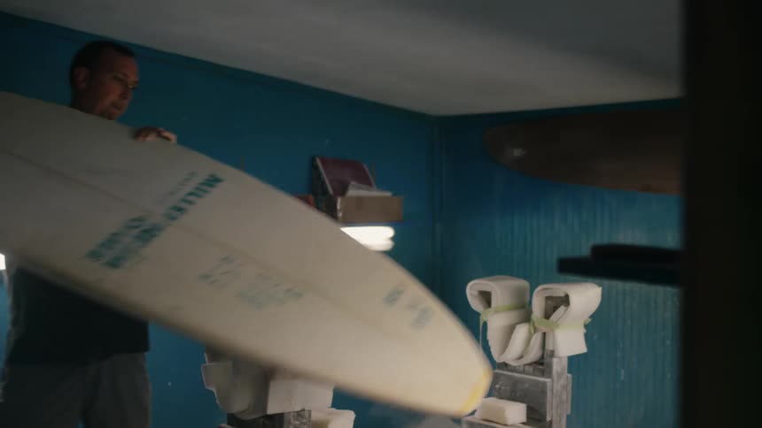 Man with black t shirt turns on light to make a surfboard in shop