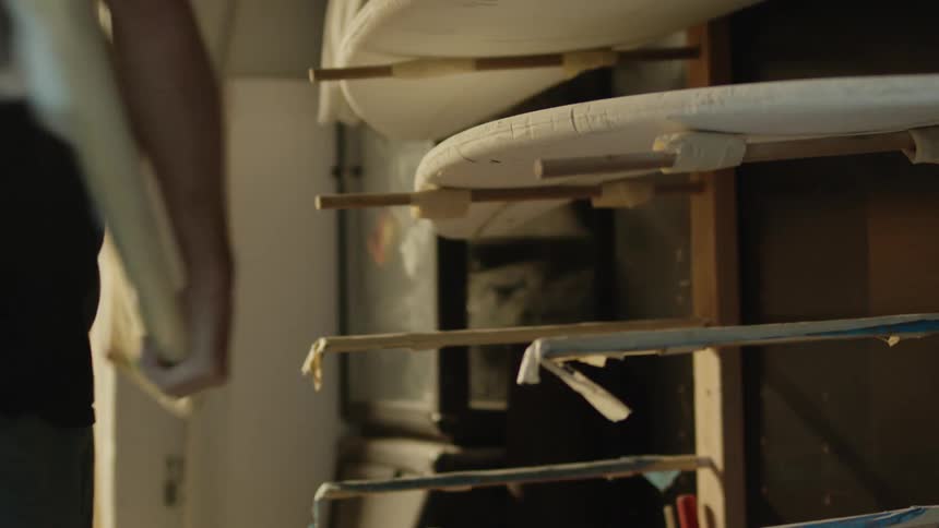 A man walks to a rack of surfboards and takes one and walks away