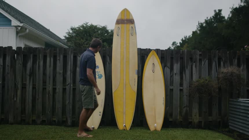 A man lines surfboards along his wooden fence in the backyard