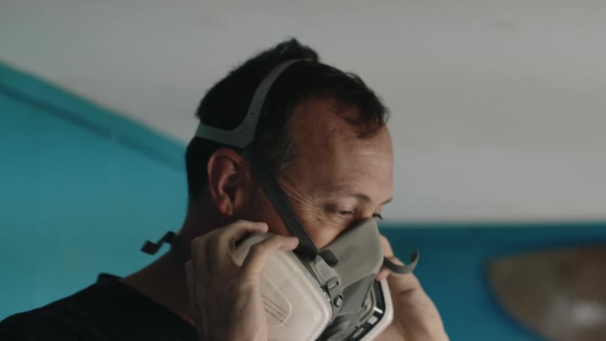 A man puts on a gas mask in a factory