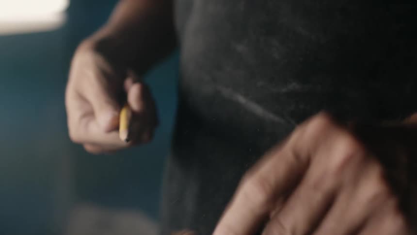 Close up of the hands of a man sharpening a pencil with a small black sharpener