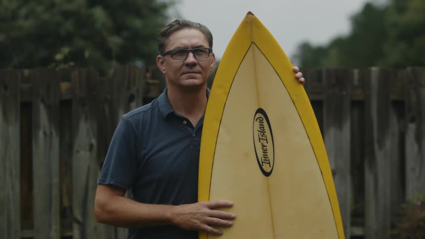 A man poses while holding a surfboard outdoors