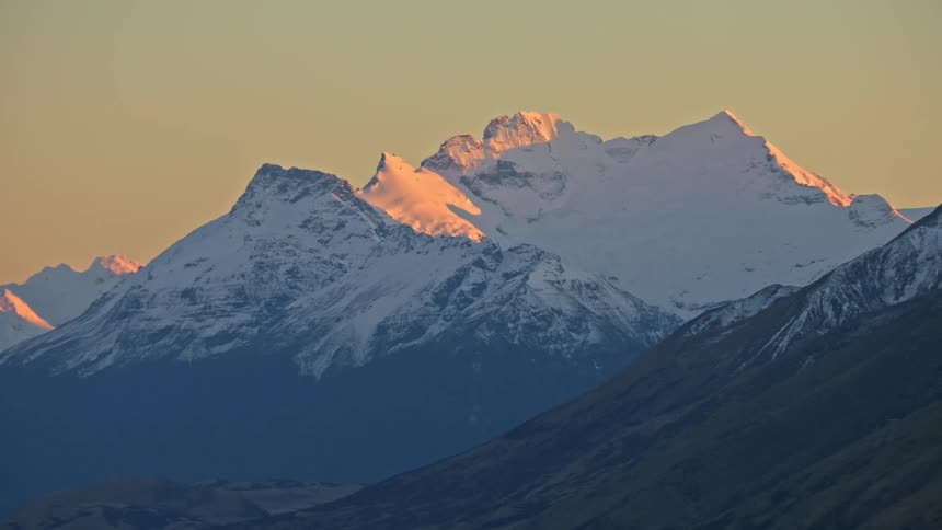 Golden sun shining on snow capped mountain ridge and peaks at dawn