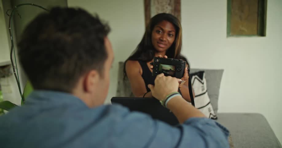 A woman shows her camera to a man who is eating