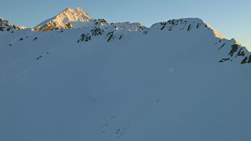 Snow covered mountains under a clear sky as the sun shines on mountains in the distance