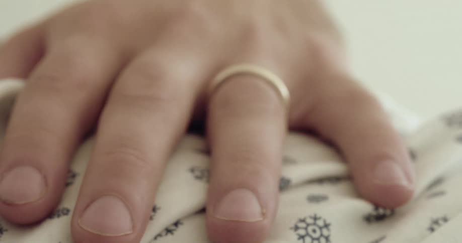 A person has their hand laying on cloth as they tap their fingers and a ring is on a finger