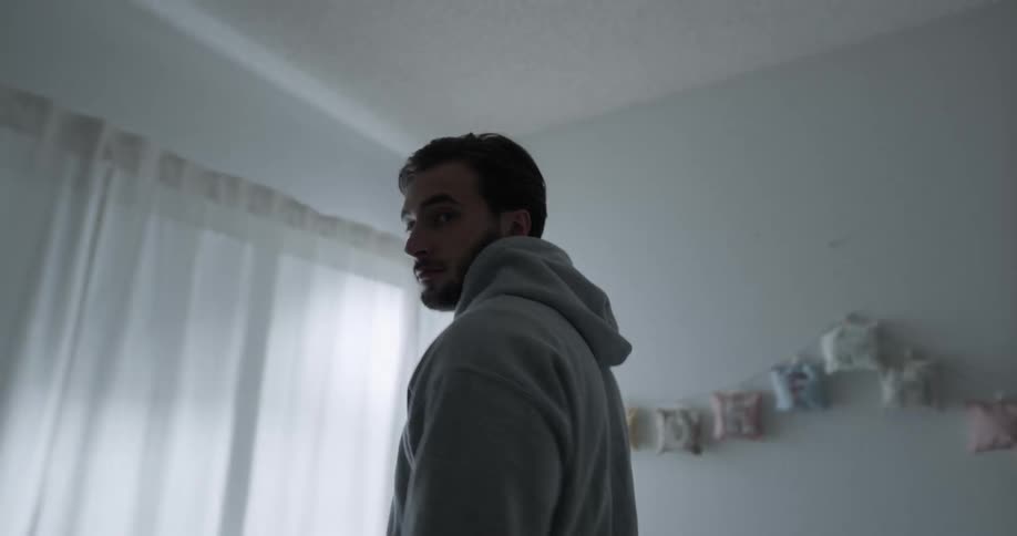 Man stands in a girls room in the dark while white lights pass by the window as he looks at the camera