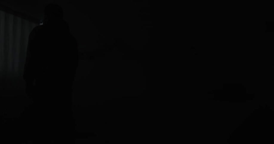 A light shines on a man in the darkness standing in a childs bedroom with ducks on the bed and alphabet letters hanging on the wall
