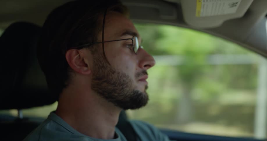 Man with beard glasses and gray t shirt drives car in the countryside