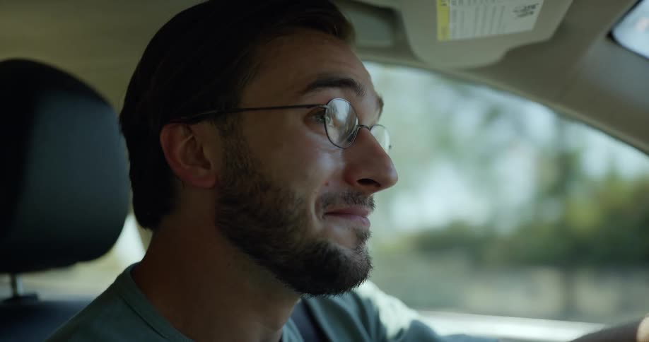 Sad man with glasses beard and shirt cries while driving car