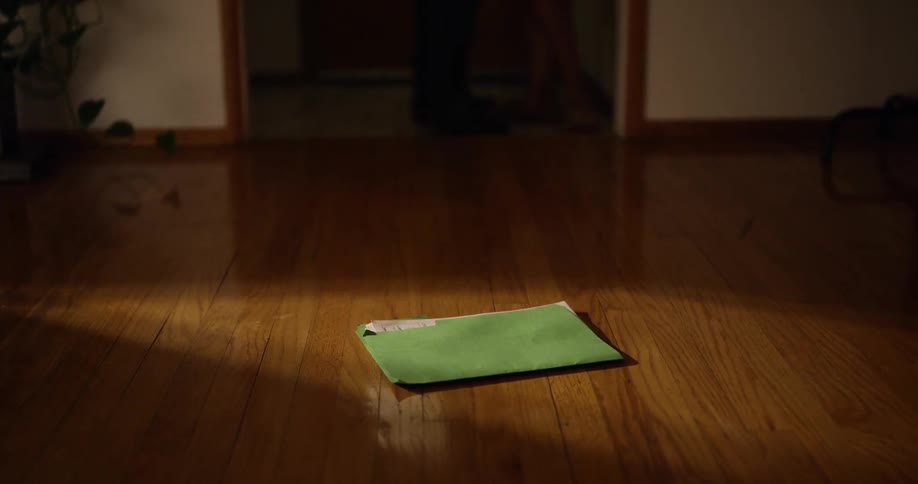 A man and a woman are walking out of a door as a green file folder sits on the hardwood floor as they leave