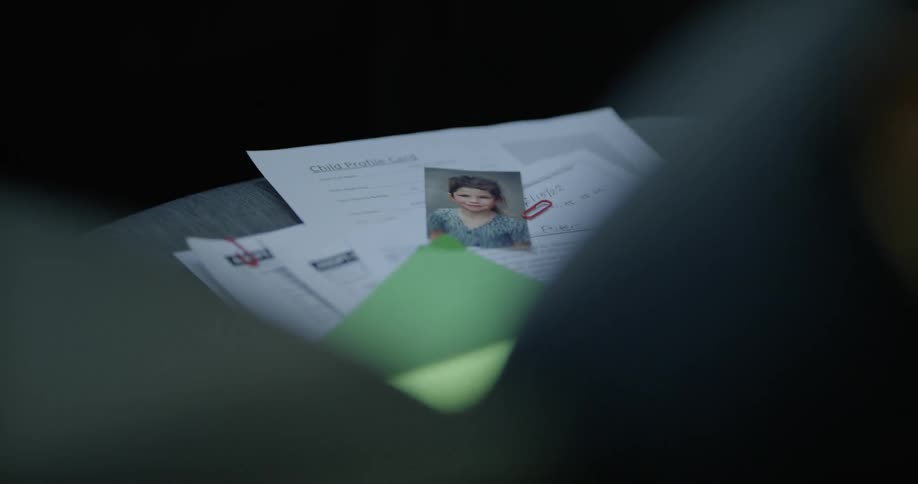 Papers held together with paperclips and a photograph of a little girl are on a table
