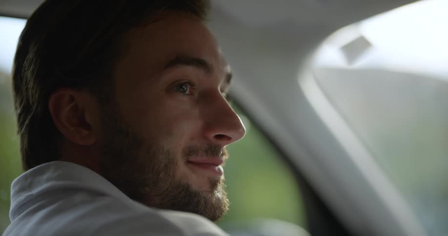 A man opens a car door and sits in the drivers seat and looks over and smiles at someone sitting in the passenger seat