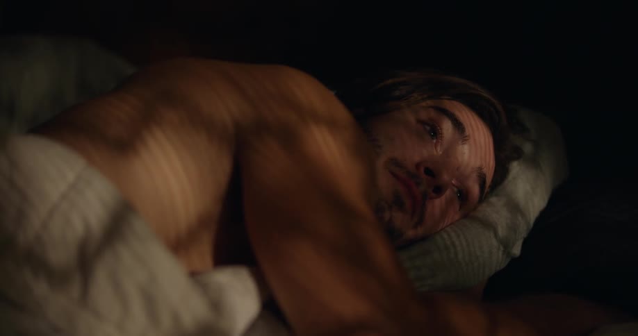 Man lying down on bed props his head onto his hand