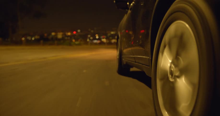 A car traveling on a road going around a curve with city lights below