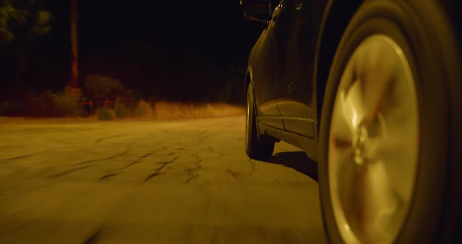 An automobile is traveling on a road with cracks in the asphalt as an oncoming car passes