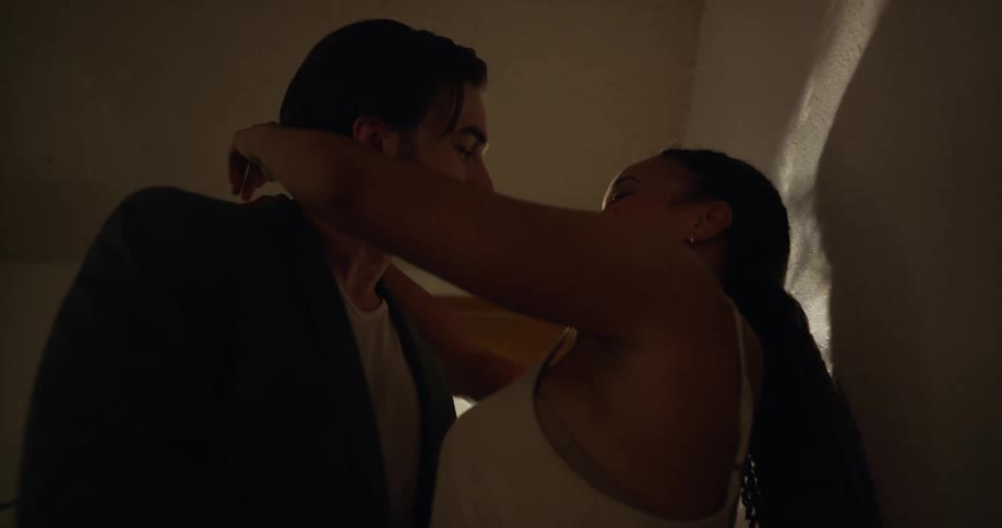 A man and a woman walk in the front door of their home and he takes her hand and they put their arms around each other and kiss by the door