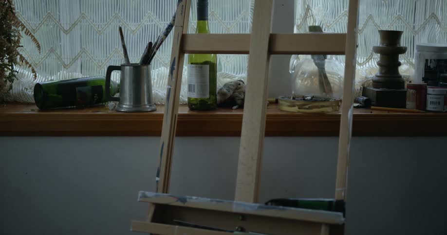 Empty easel with paint stains standing on a painters studio near a shelf under a window