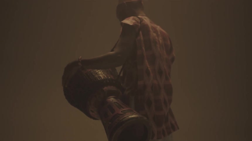 A man holding a bongo against his side as he stands in a dark area