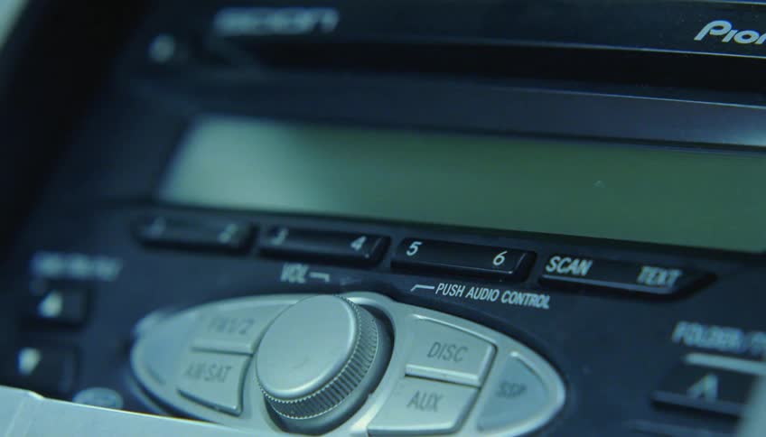 A finger presses a button turning a car radio on