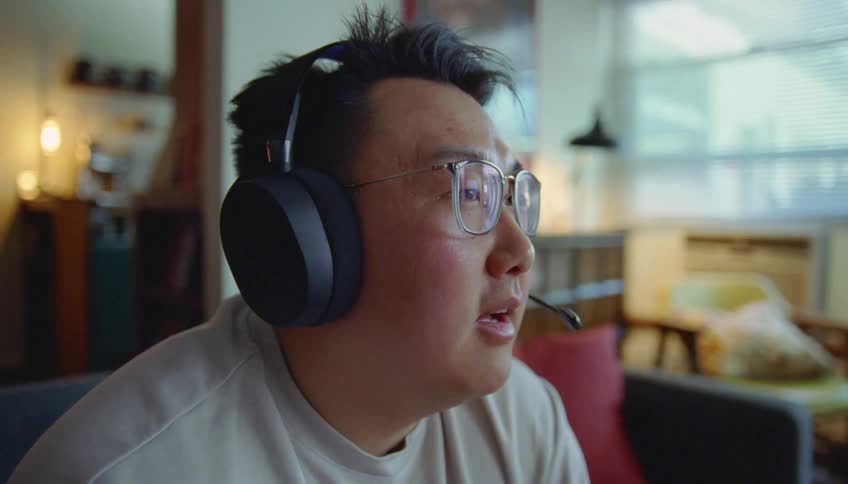 Man with glasses gray sweatshirt and headset talks to person in the living room