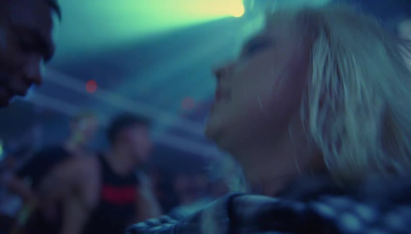Man wearing wooly hat and blonde woman dance in nightclub shaking heads