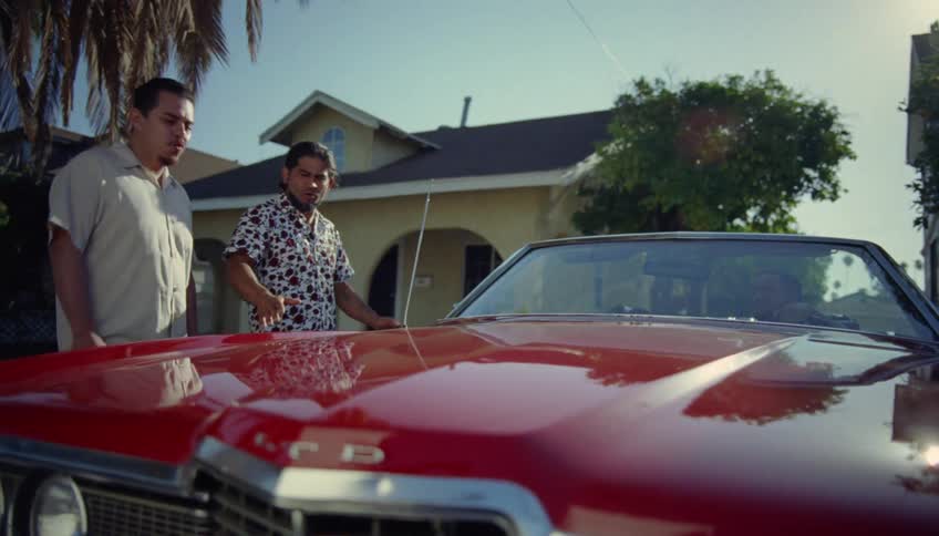 Two men talk and look at a red car