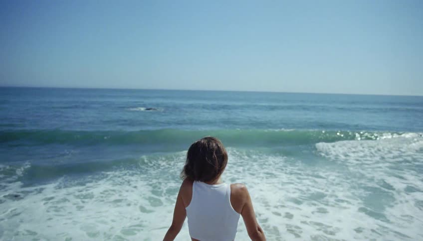 A woman sits on the beach right along the coast