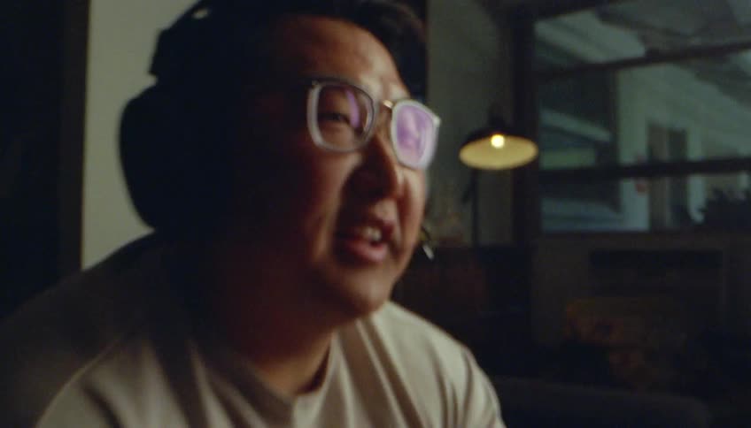 An asian mean wearing thick eyeglasses is speaking into a microphone on his headset