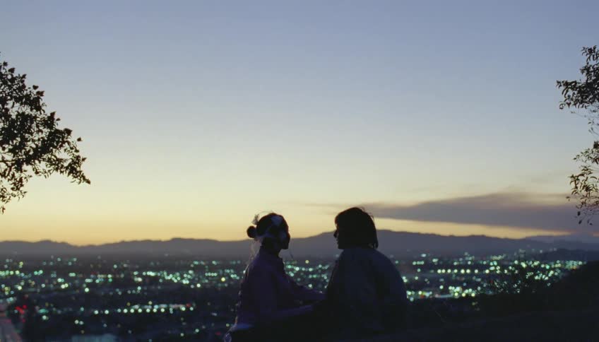 Silhouette of a young couple kissing and talking in front of a city at evening