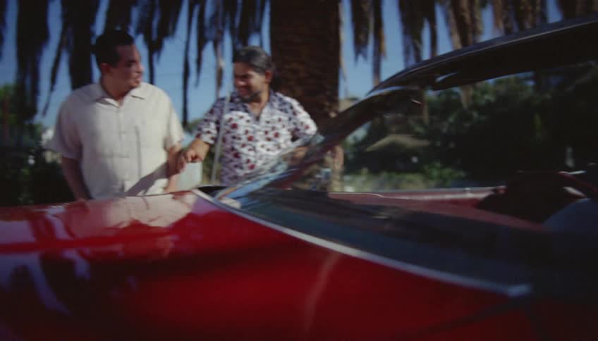 A man sitting behind the wheel of a shiny red convertible talks to his friends