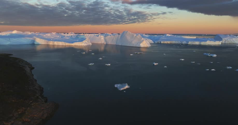 Chunks of ice and icebergs floating near land under a cloudy and golden sky