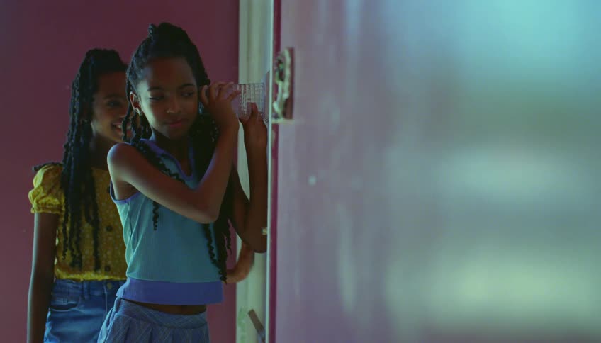 Curious girls listen to a conversation on the other room using a glass pressed against the door