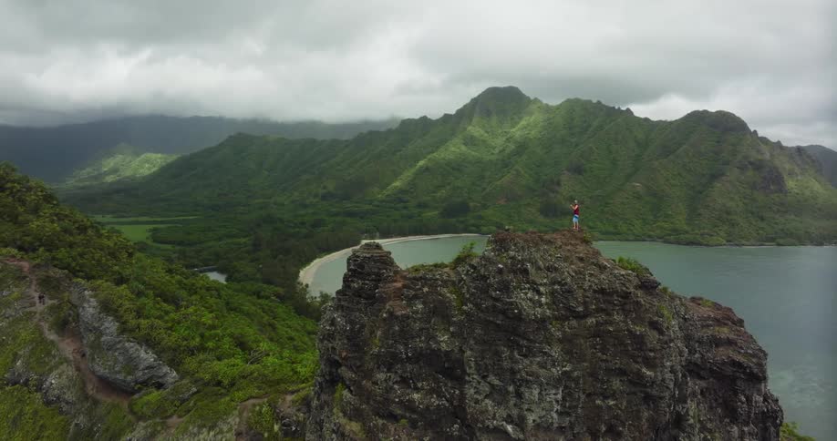 Aerial view of a man standing on top of a promontory in the mountains next to a bay