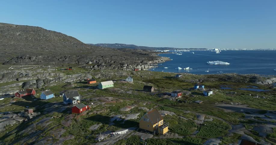 Small icebergs float in water near small town surrounded by green vegetation
