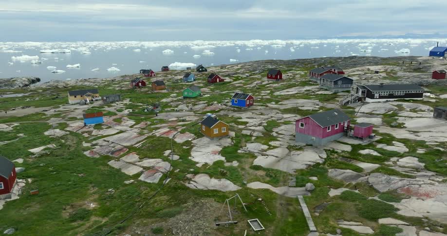 A neighborhood made up of colorful single family homes sits along an ice filled ocean