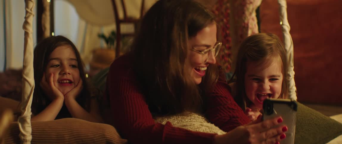 Mother laying in the floor of the living room with her daughters looking at funny videos on the smartphone