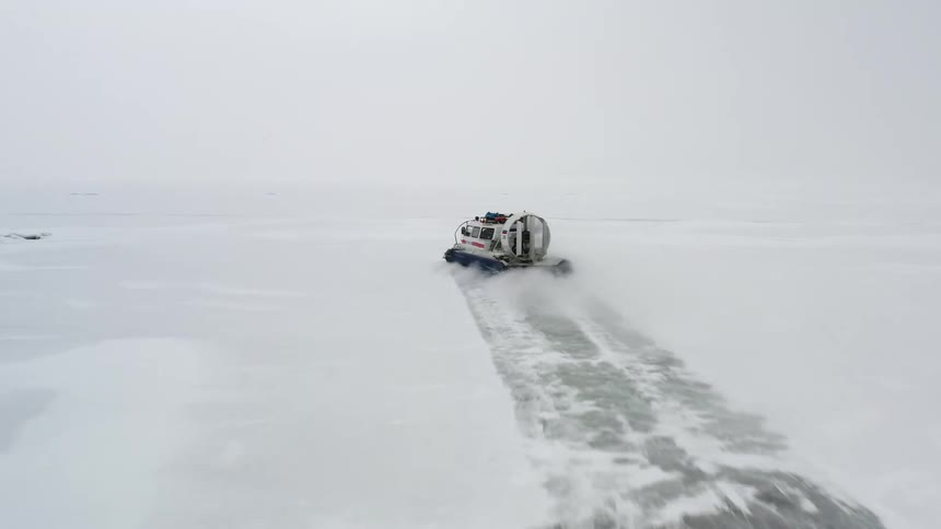 A machine drives across a snowy field and blows the snow