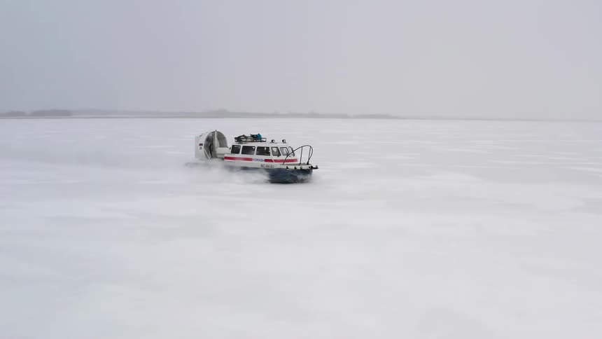 A hovercraft travels over ice leaving a trail as it kicks up snow on a gray cloudy day