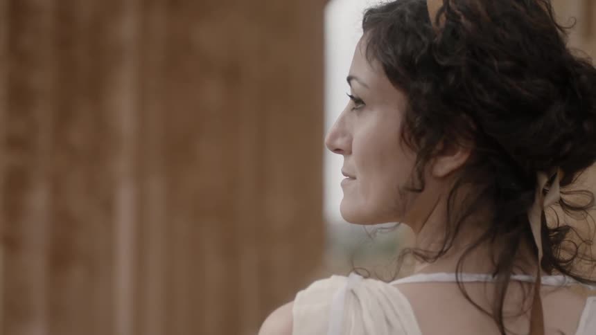 A breeze blowing a woman's hair as she stands next to stone columns
