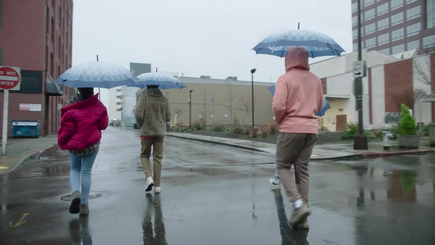 A group of people holding umbrellas walk together down a city street on a rainy day