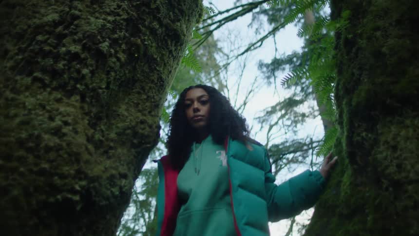 Woman poses between two trees in forest in a color coordinated outfit