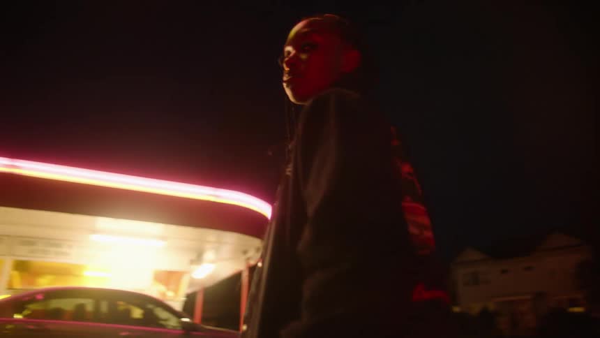 A girl standing in a restaurant parking lot at night looking around for her friends