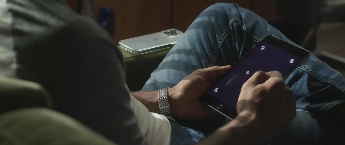 A man is sitting down holding a tablet with white symbols on the screen