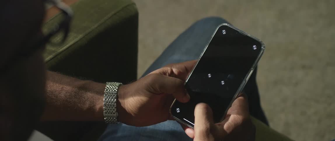 A man is sitting typing on a smartphone with white symbols on the screen