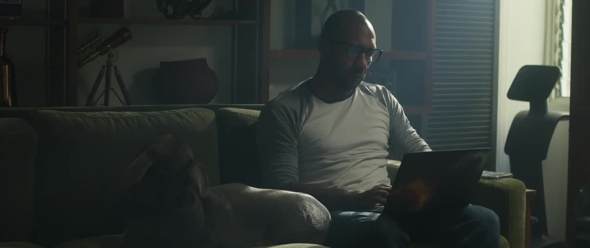 A man pets his dog while using a laptop