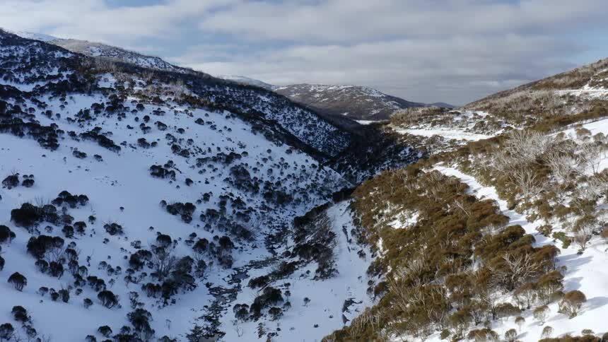 Aerial view of a river flowing between the snow covered slopes of a mountain range at morning
