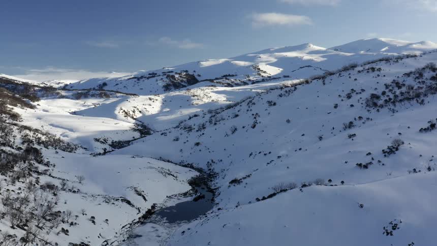 Shadows cover most of snowy slopes in river valley stretching to mountains on the horizon