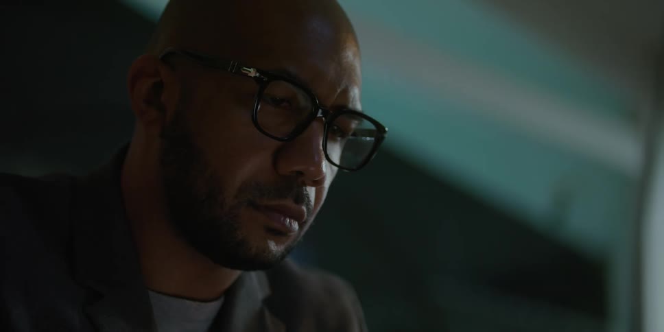 Man with shaved head glasses beard and green blazer jacket uses laptop in the living room
